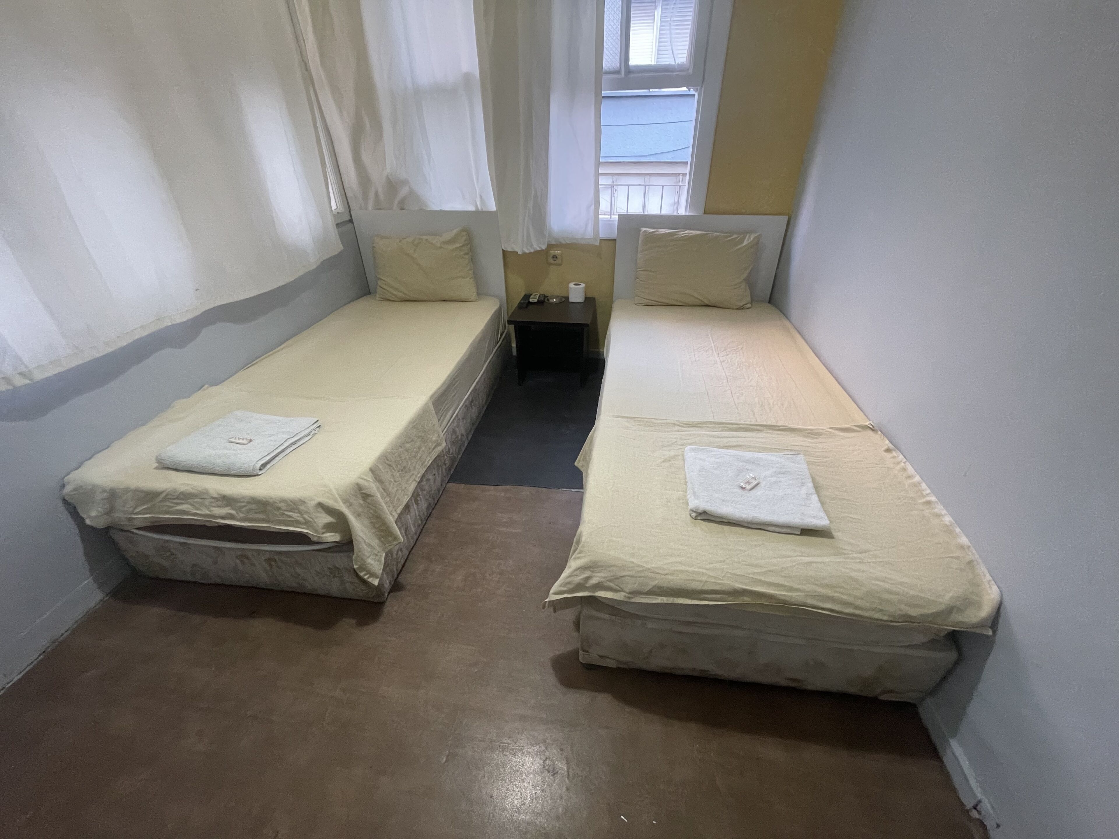A small, narrow room with two single beds, each with a pillow and a folded towel.