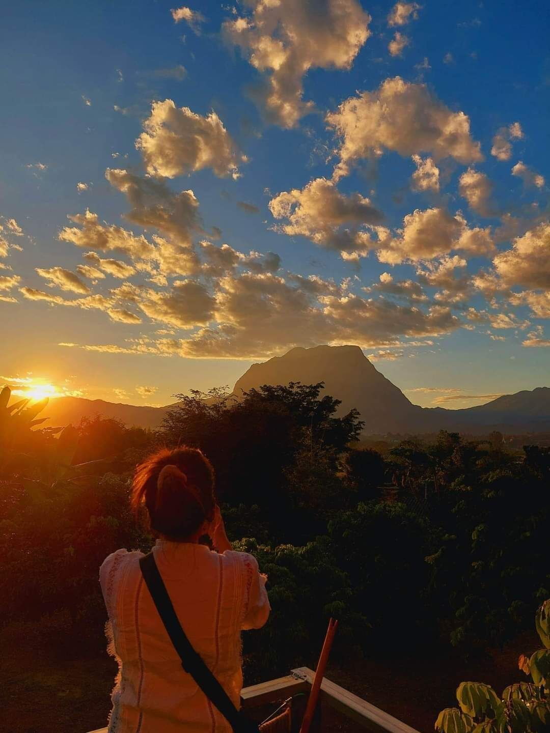 A person taking a photo of a sunset with a mountain in the background.