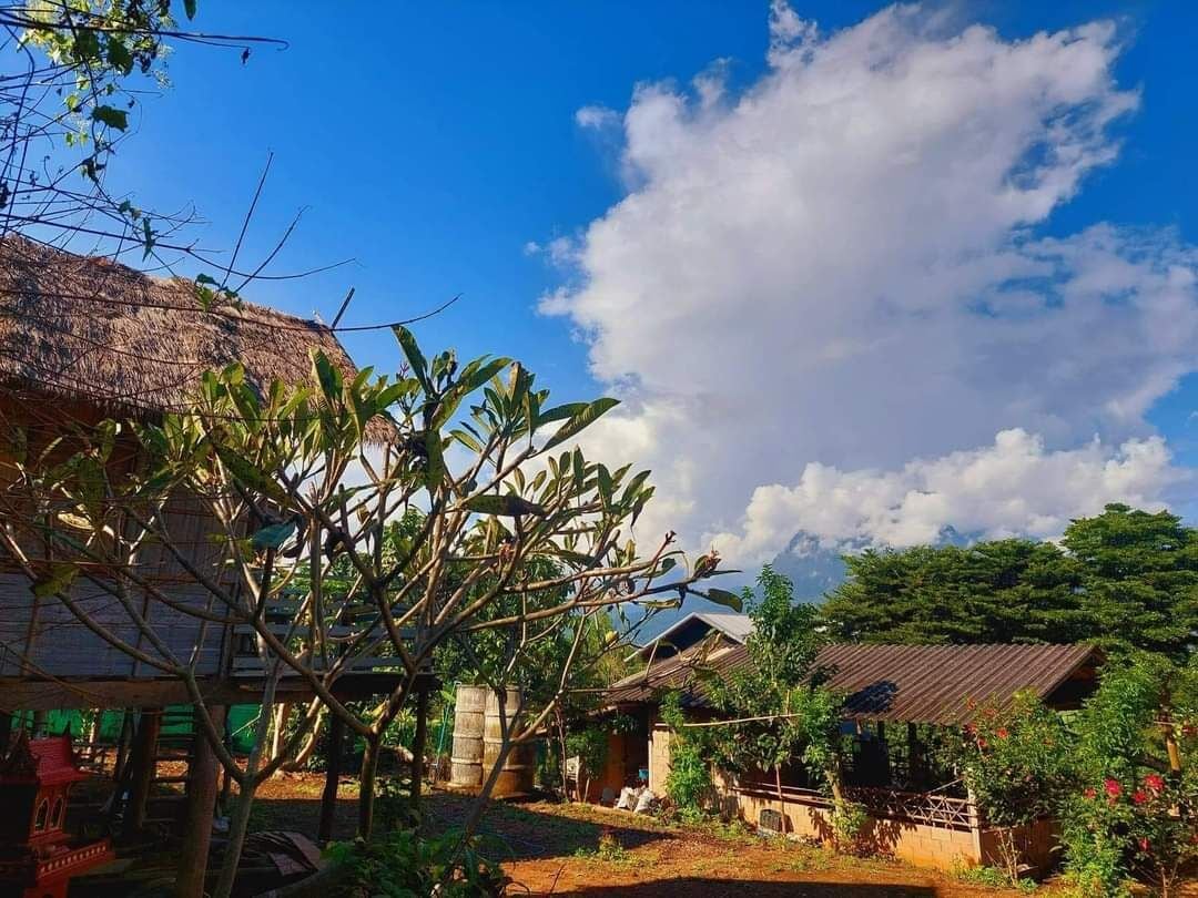 A rural village with traditional thatched-roof houses, surrounded by lush greenery and a clear blue sky.