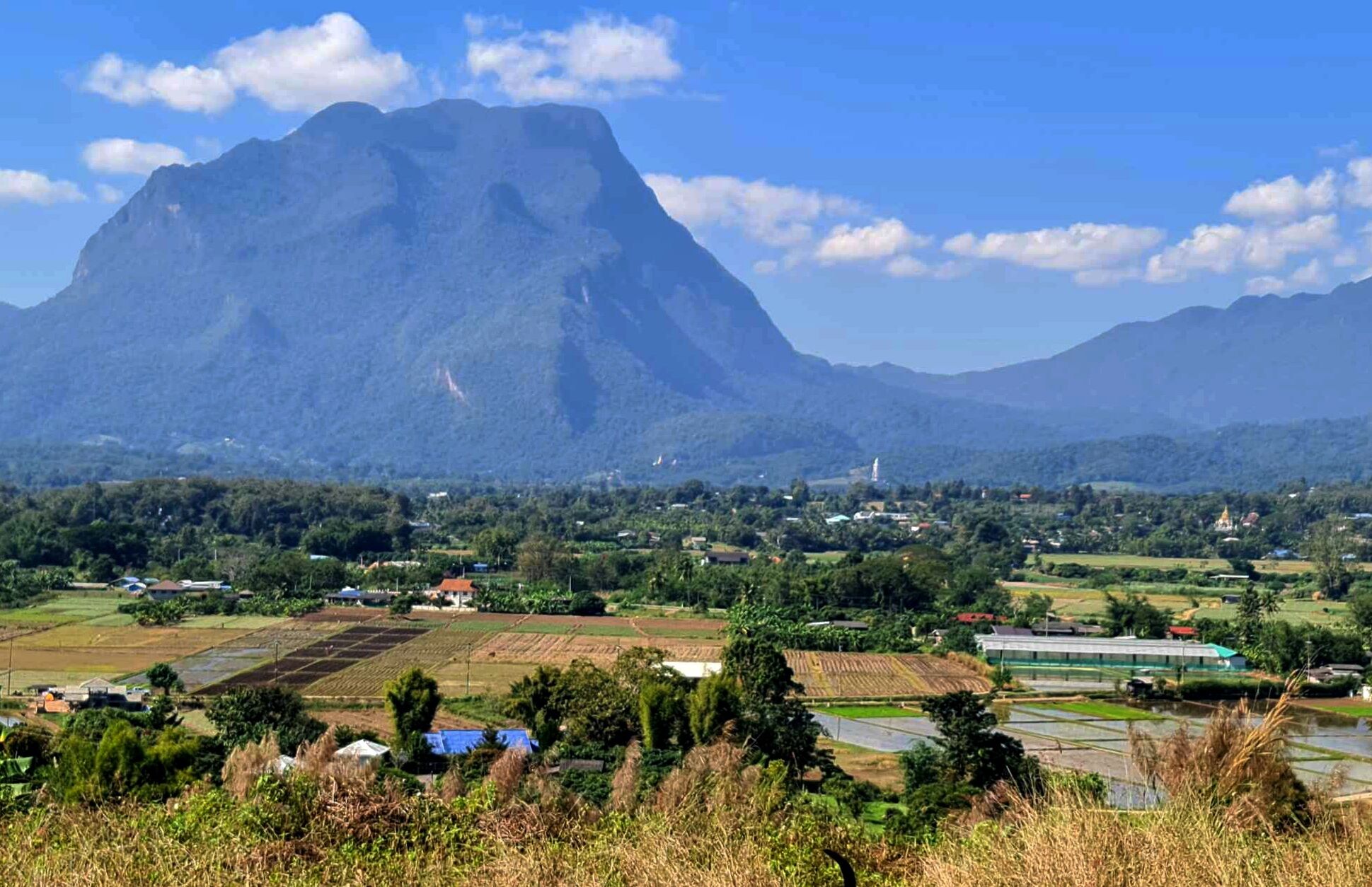A mountainous landscape with a village in the foreground featuring agricultural fields and a few buildings.