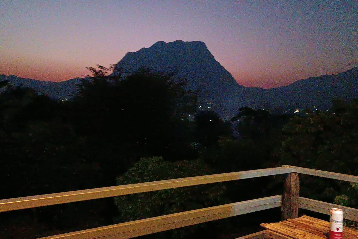 A bench with a can of drink on it, overlooking a mountainous landscape with a sunset.
