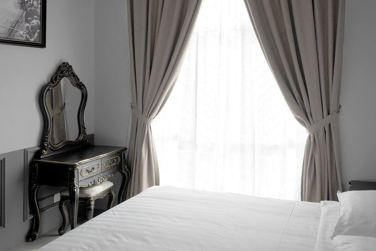 A room with a bed, a dresser with a mirror, and sheer curtains.