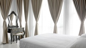 A bedroom with a large bed, a dresser with a mirror, and sheer curtains. - Zetter Suites (Tanah Rata)
