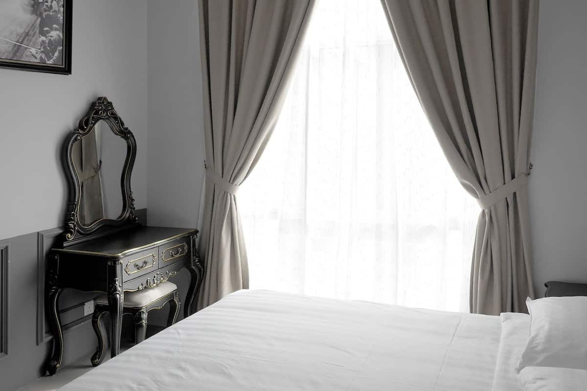 A room with a bed, a dresser with a mirror, and sheer curtains.