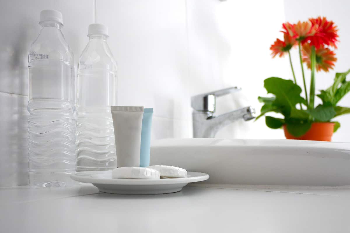 A bathroom with a sink, two water bottles, a soap dish, and a potted plant with flowers.