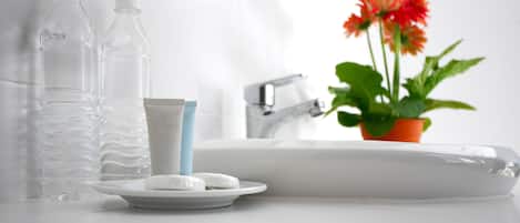 A bathroom with a sink, two water bottles, a soap dish, and a potted plant with flowers.