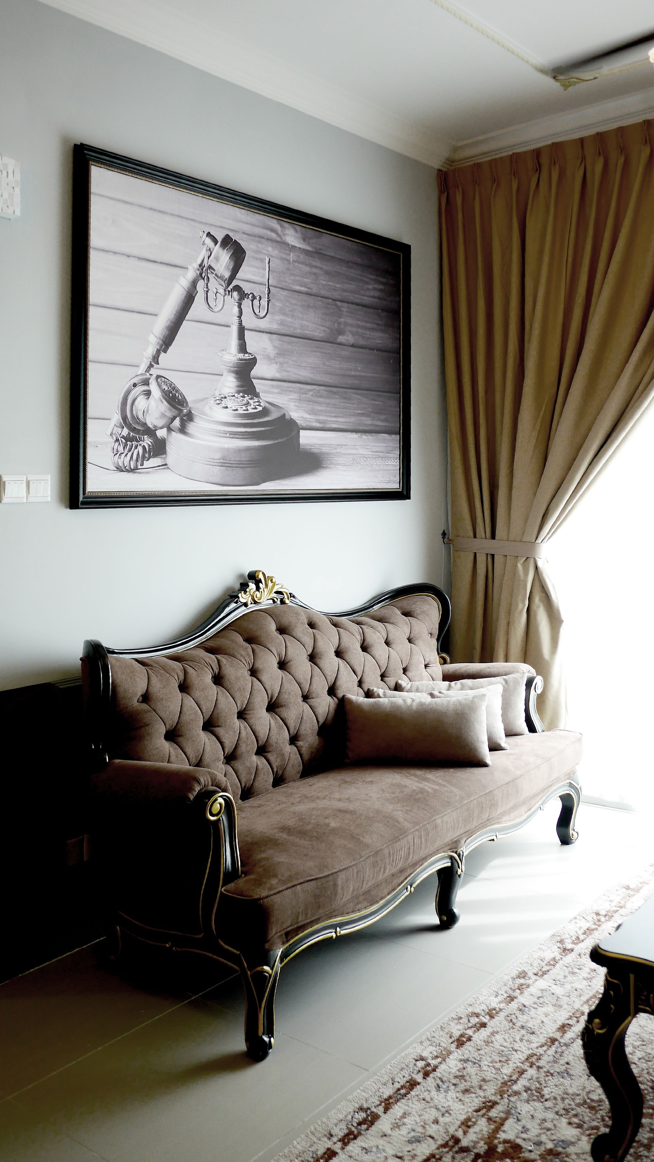 Une pièce avec un canapé marron capitonné, une photographie en noir et blanc encadrée accrochée au mur et une fenêtre ornée de rideaux beige.
