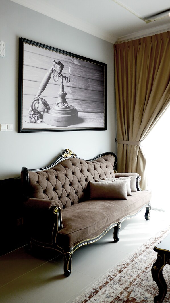 A room with a tufted brown sofa, a framed black and white photograph on the wall, and a window with beige curtains.