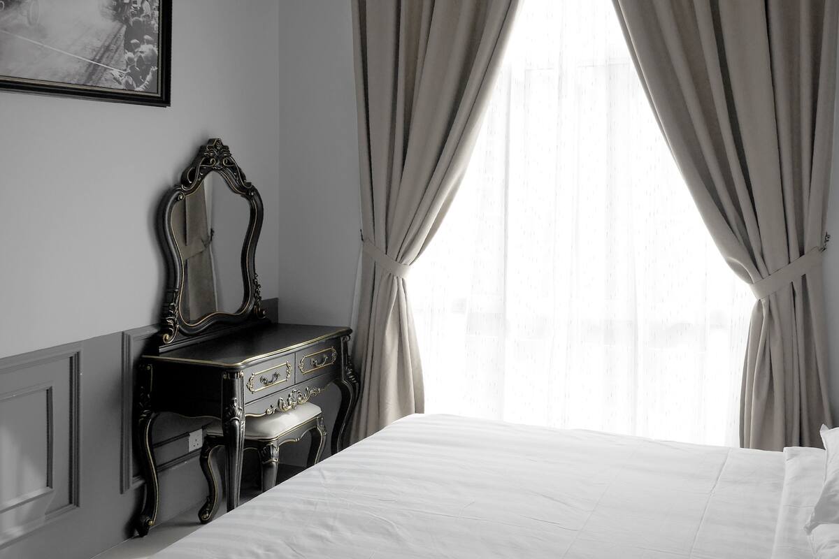 A bedroom with a bed, a dresser with a mirror, and a window with curtains.