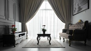 A room with a sofa, a table with a plant, a TV, and a painting on the wall. - Zetter Suites (Tanah Rata)