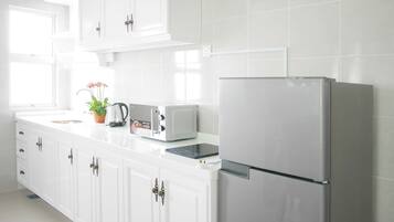 Une cuisine moderne avec des meubles blancs, un réfrigérateur en acier inoxydable, un grille-pain et une bouilloire.