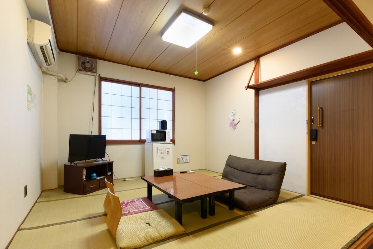Quarto tradicional japonês com tatames, televisão, micro-ondas e porta de correr.