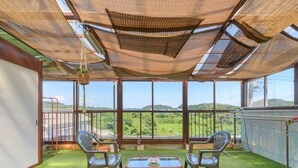 Ein Wintergarten mit Blick auf eine üppige Landschaft, möbliert mit Korbstühlen und einem Glastisch.