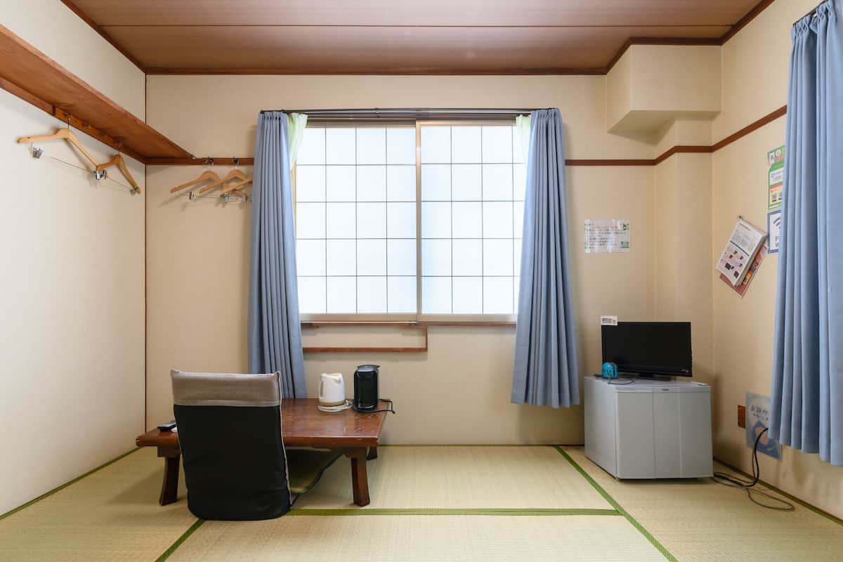 Quarto com piso de tatame, uma mesa baixa com uma cadeira, televisão, chaleira e armário.