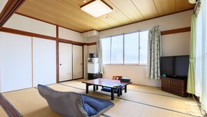 Ein Raum mit Tatami-Matten, einem Futon, einem Tisch, Stühlen, einem Fernseher und einem Schrank.