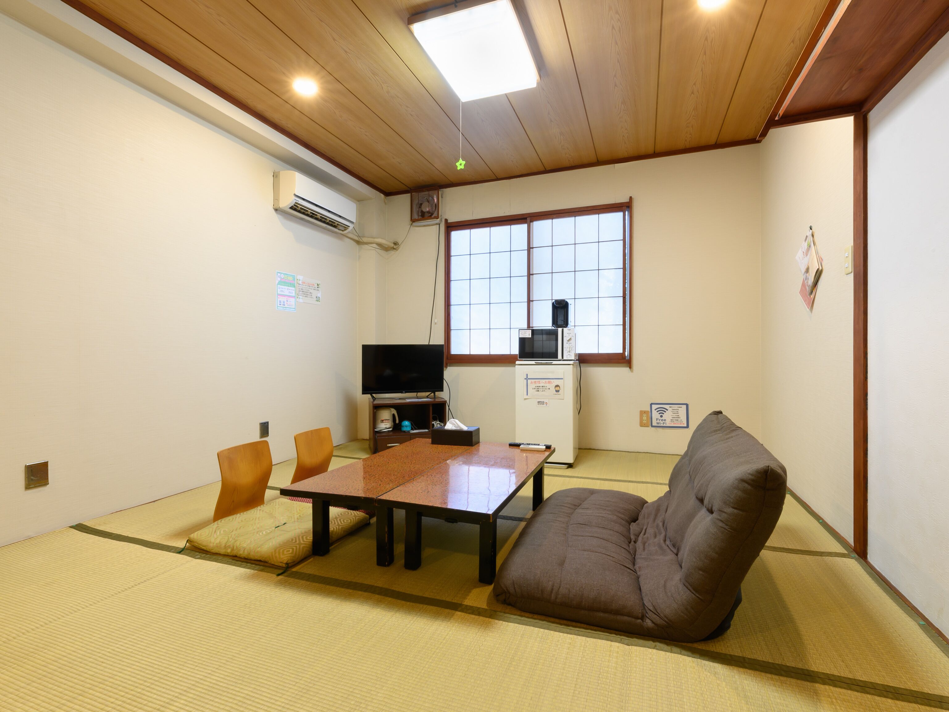 A traditional Japanese room with tatami flooring, a low table, a sofa, and a TV on a small cabinet.