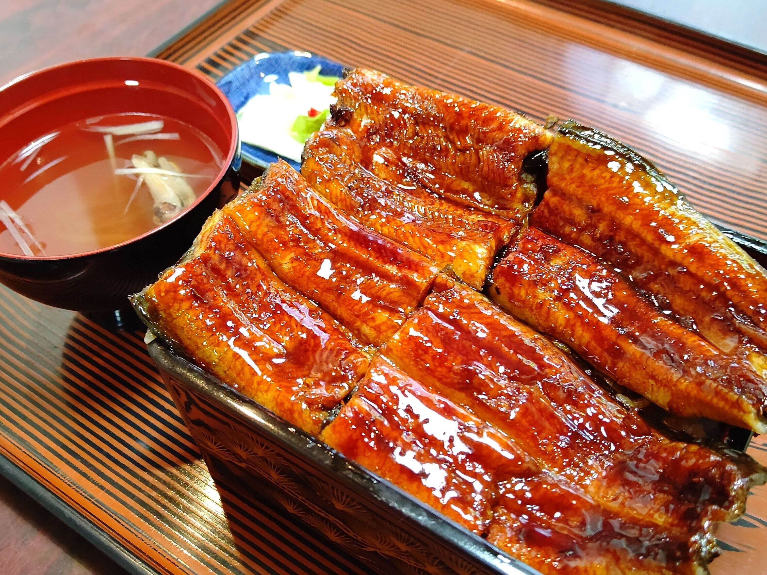 A tray of glazed fish slices, a small bowl of soup, and a small dish of pickled vegetables.