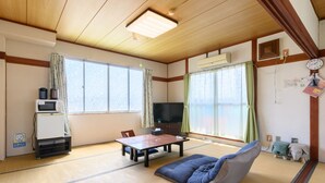 Ein traditioneller japanischer Raum mit Tatami-Böden, einem niedrigen Tisch, einer Couch, einem Fernseher und einem Kühlschrank.