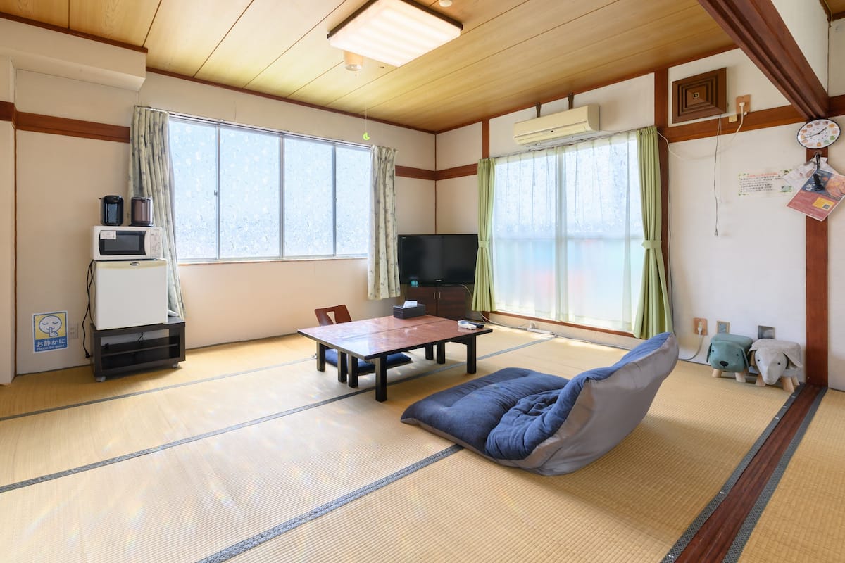Um quarto em estilo japonês tradicional, com tatames, uma mesa baixa, um sofá, uma televisão e um frigorífico.