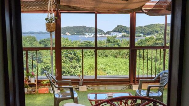 Ein Balkon mit Korbstühlen und einem Tisch mit Blick auf ein Gewässer und Grünflächen.