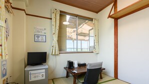 Ein Zimmer mit Fernseher, Schreibtisch mit Wasserkocher, Stuhl und einem fenster mit Vorhängen.