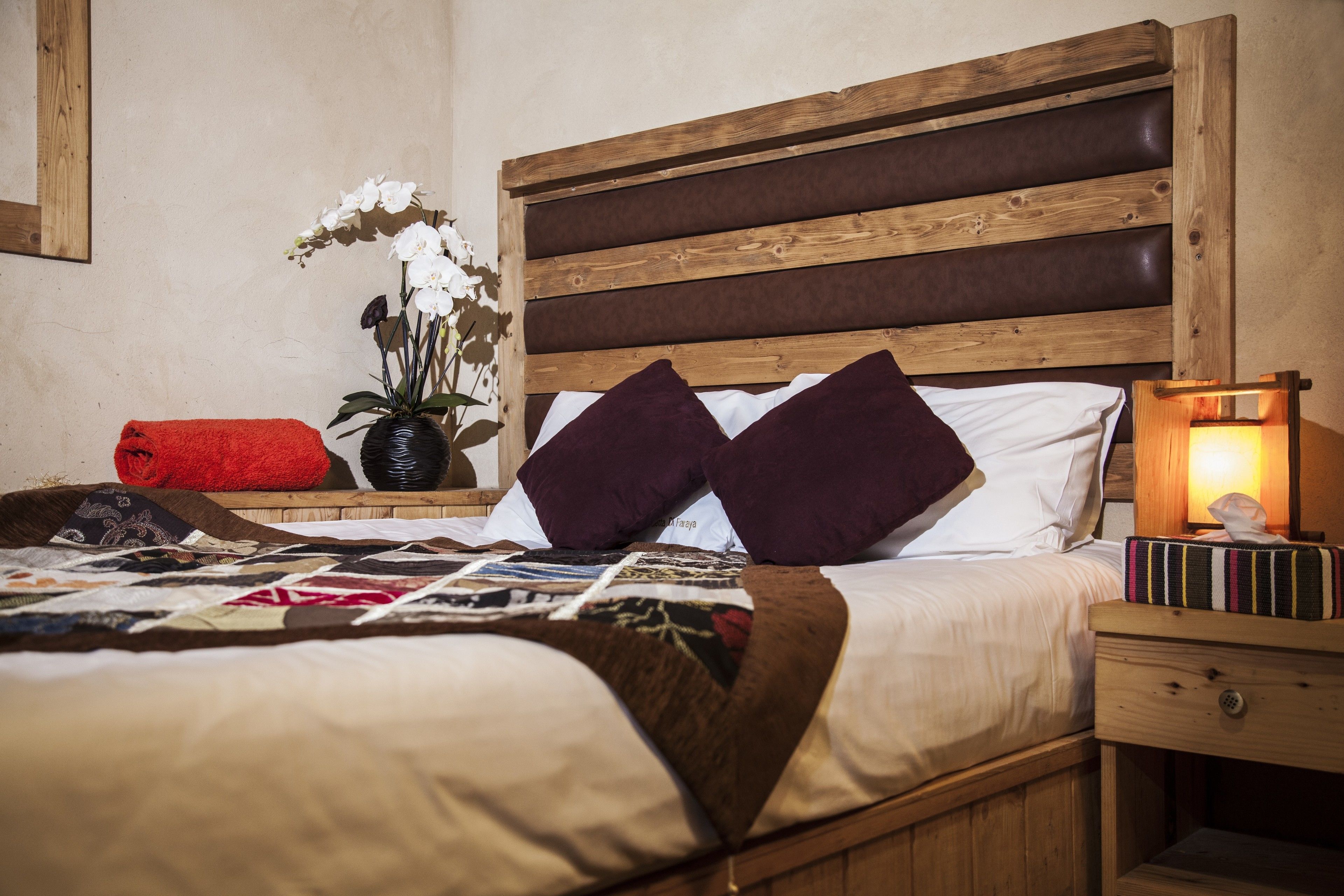 A neatly made bed with a quilt, pillows, and a bedside table with a lamp and books.
