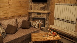 A cozy room with a stone fireplace, a flat-screen TV mounted above it, a sofa with patterned cushions, and a wooden coffee table with glasses and a remote control. - Villetta Di Faraya (Faraya)