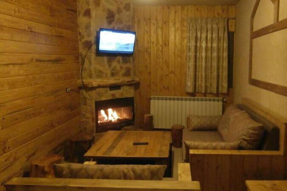 Una habitación acogedora con una chimenea de piedra, un televisor montado en la pared y un sofá de madera.