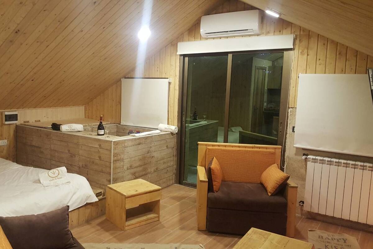 Una habitación acogedora de madera con una cama, una mesita, un sofá y un ventanal corredero que da a un balcón.