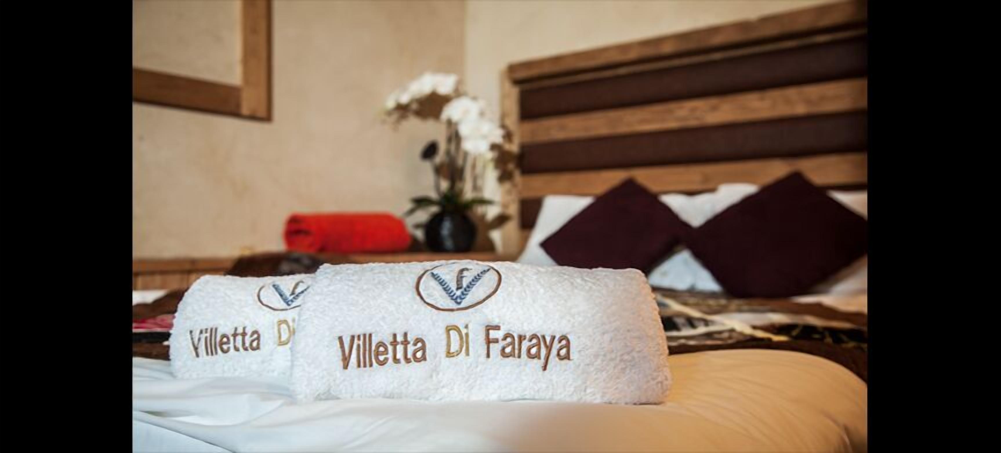 Ein ordentlich bezogenes Bett mit zwei Handtüchern mit dem Aufdruck "Villetta Di Faraya" und einer Vase mit weißen Blumen auf dem Nachttisch.