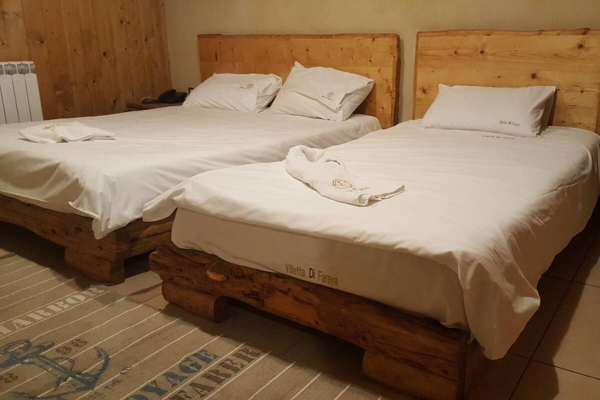 Dos camas de madera con ropa de cama y almohadas blancas, una mesita de noche de madera y un suelo de baldosas.