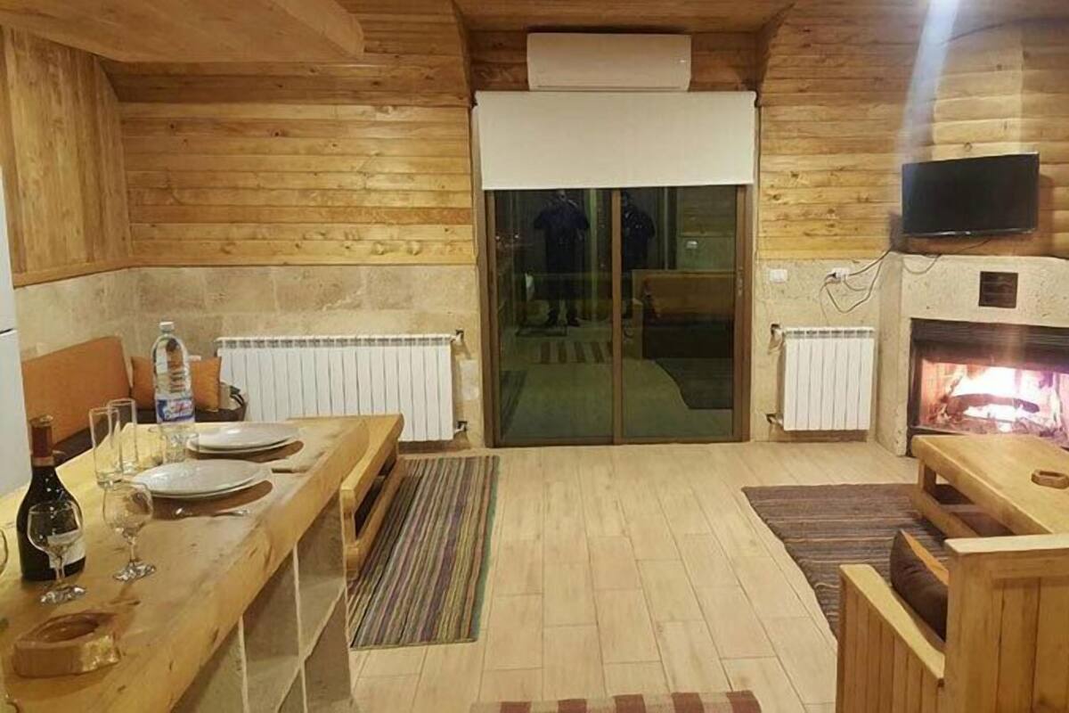 Interior acogedor de una cabaña de madera con comedor, chimenea y televisor montado en la pared.