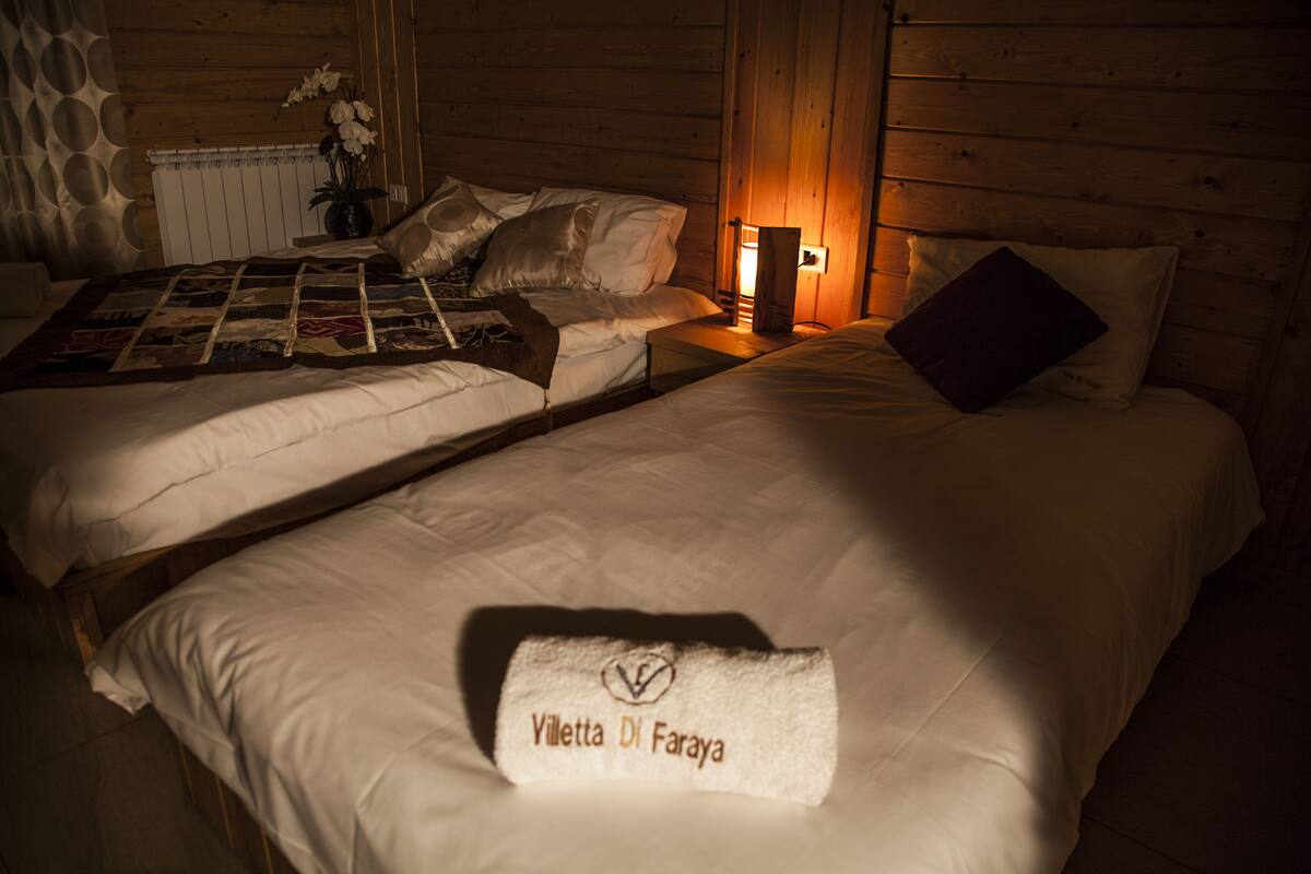 Una habitación con dos camas, una mesita de noche con lámpara y un edredón en la cama de la izquierda.