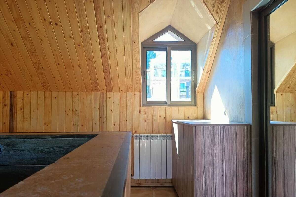 Un interior de madera con techo inclinado, una ventana y un radiador.