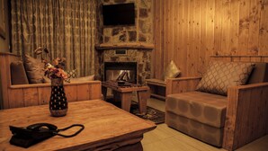 A cozy room with a stone fireplace, wooden furniture, and a television mounted on the wall. - Villetta Di Faraya (Faraya)