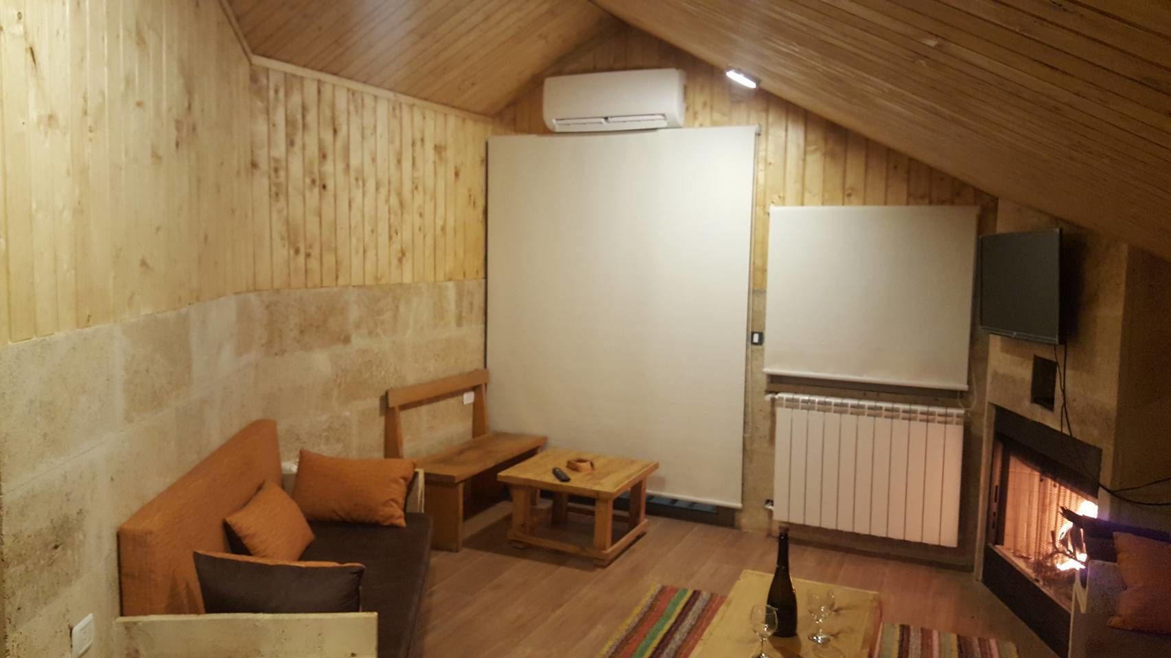 Une pièce mansardée chaleureuse avec des murs en bois, un canapé, une petite table, une cheminée et un téléviseur fixé au mur.