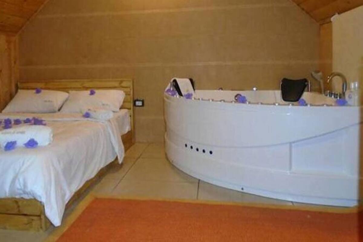 Una habitación con dos camas, una bañera grande y techo de madera.