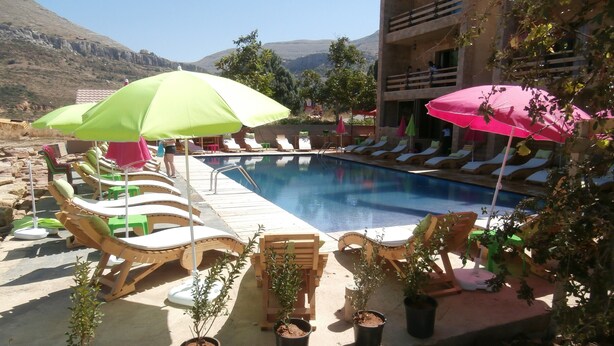 A poolside area with lounge chairs and umbrellas, surrounded by potted plants and a building in the background. - Villetta Di Faraya (Faraya)