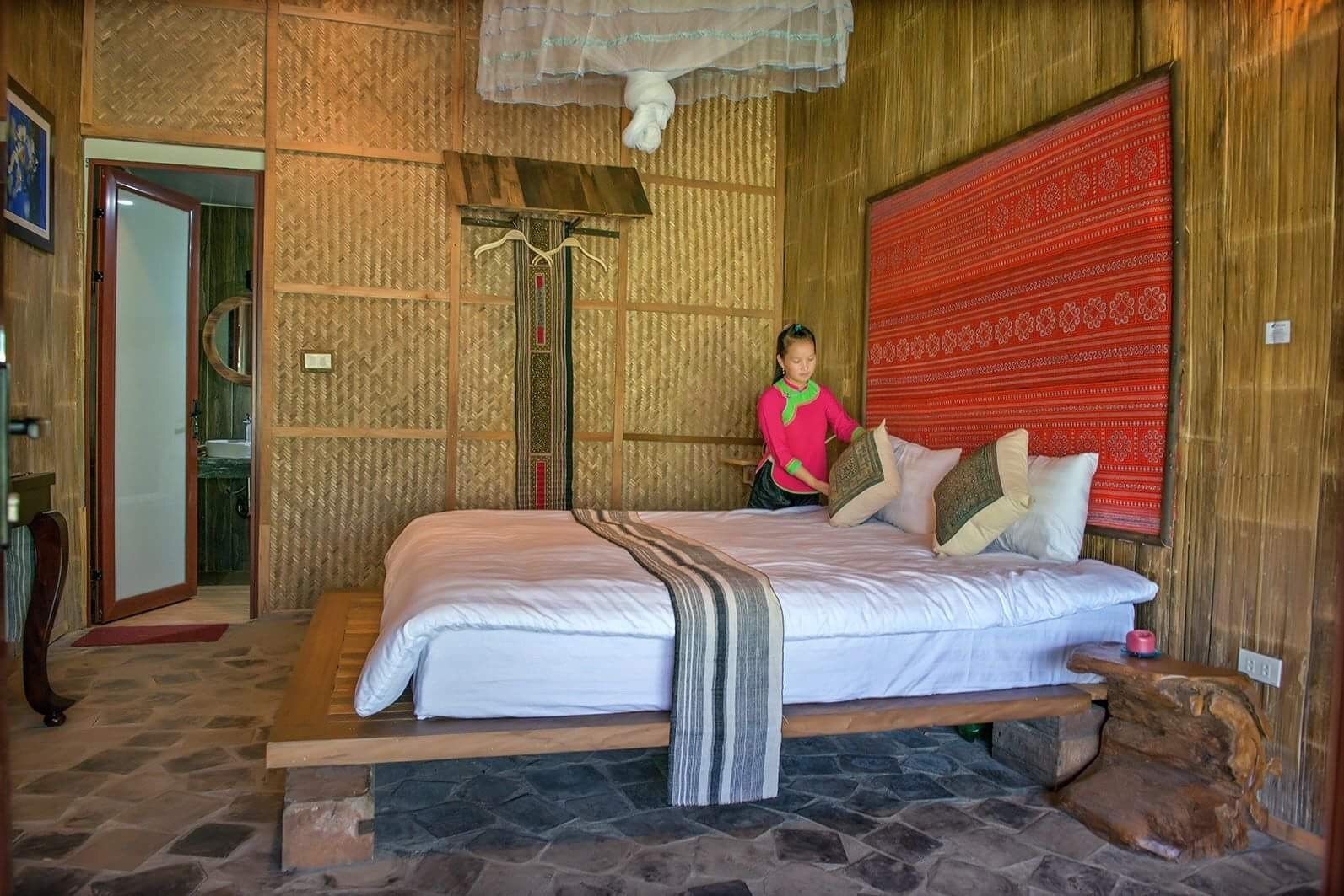 A bedroom with a large bed, a wooden headboard, a red patterned tapestry, and a stone floor.