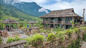 A rustic outdoor seating area with wooden tables and chairs, surrounded by lush greenery and a mountain backdrop. - La Dao Spa Homestay (Ta Van)