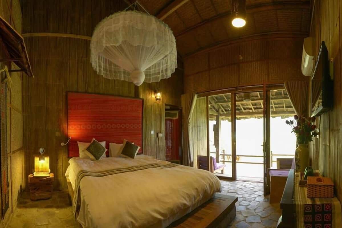 A spacious bedroom with a large bed, a wooden floor, a red headboard, and a view of the outdoors.