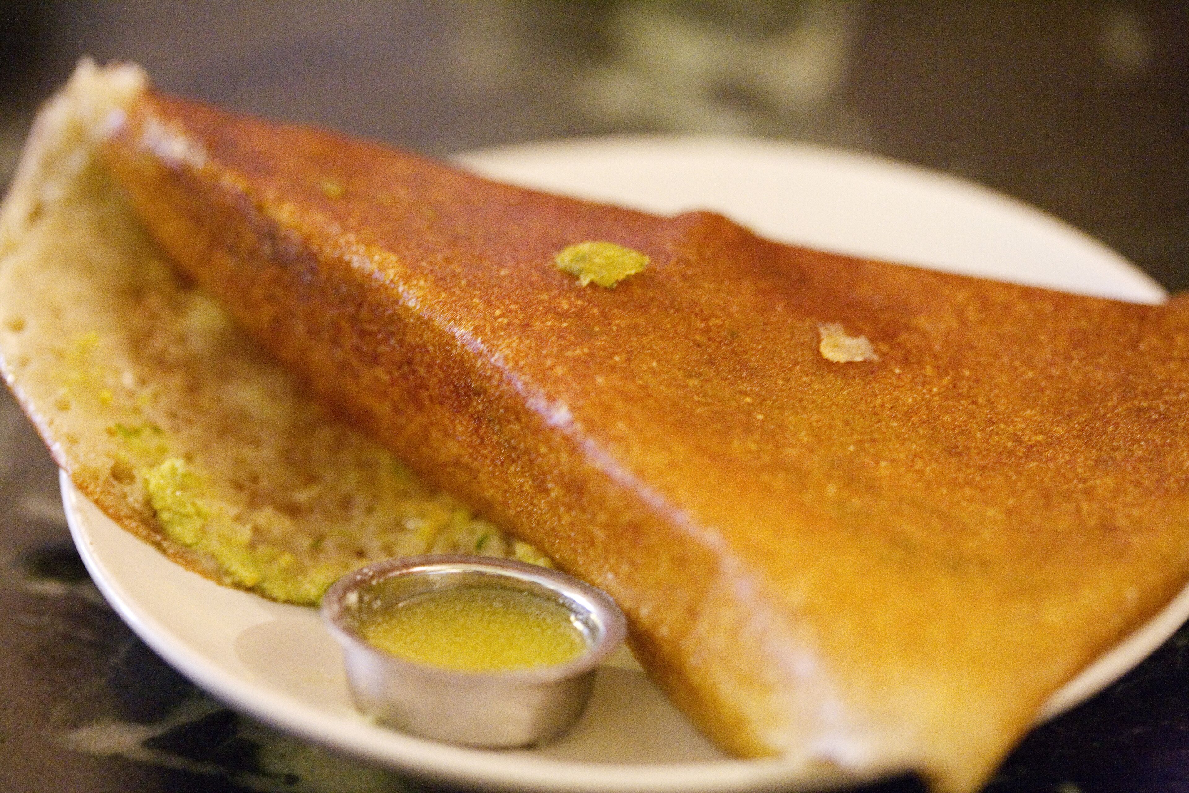 A folded crepe with a side of green sauce on a white plate.