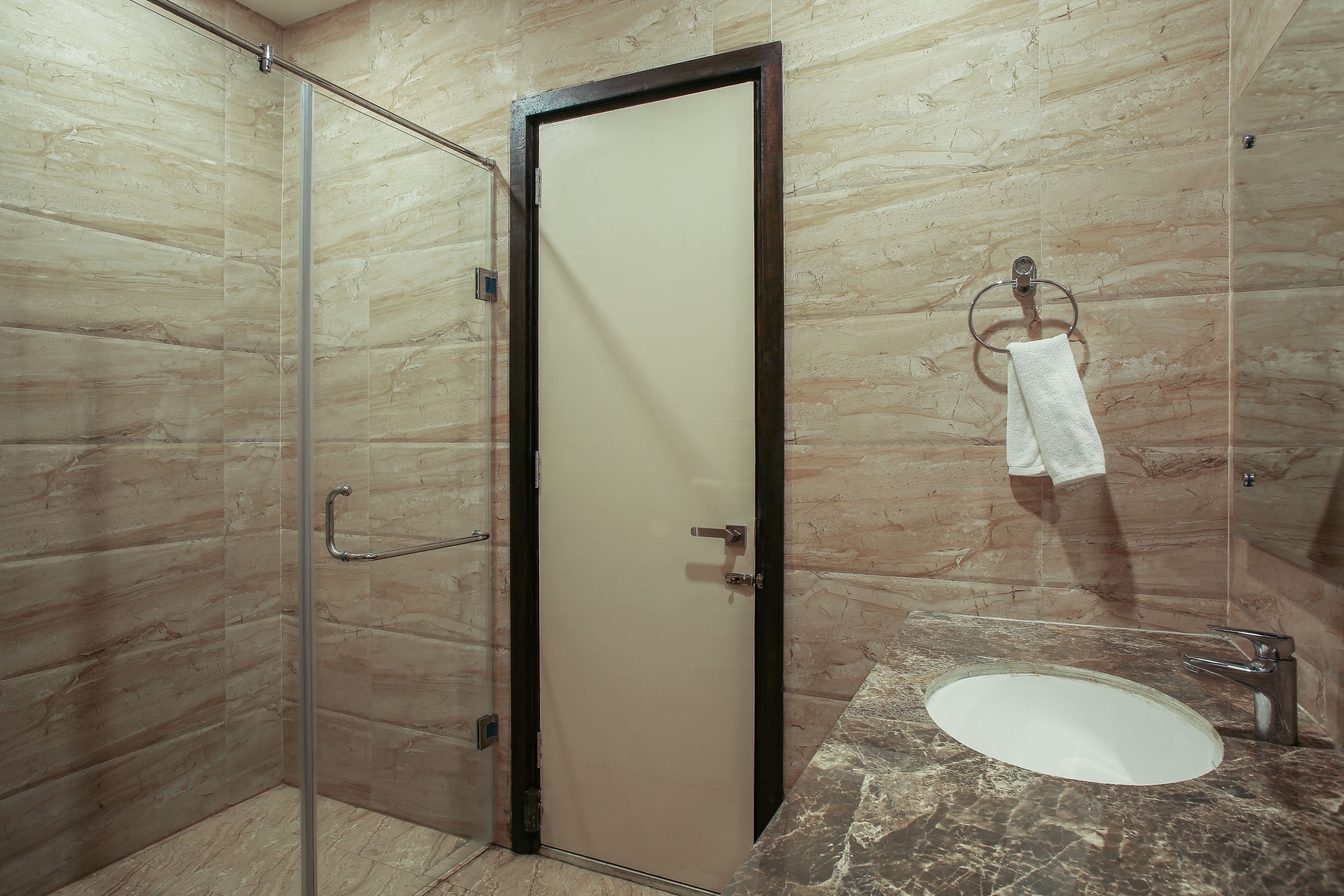 A bathroom with a glass shower enclosure, a white door, and a marble countertop with a sink.