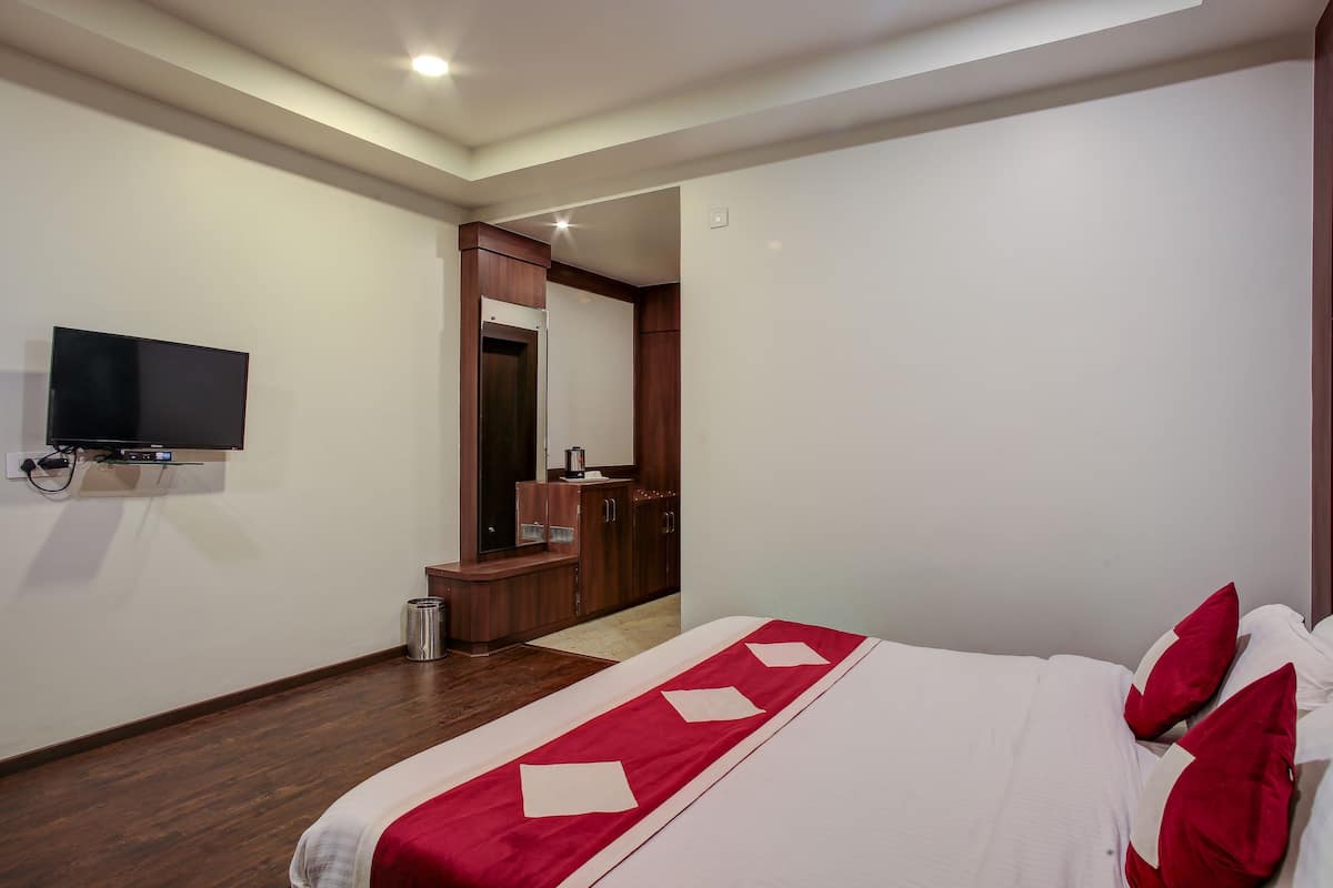 A hotel room with a bed, a TV mounted on the wall, a wooden cabinet, and a mirror.