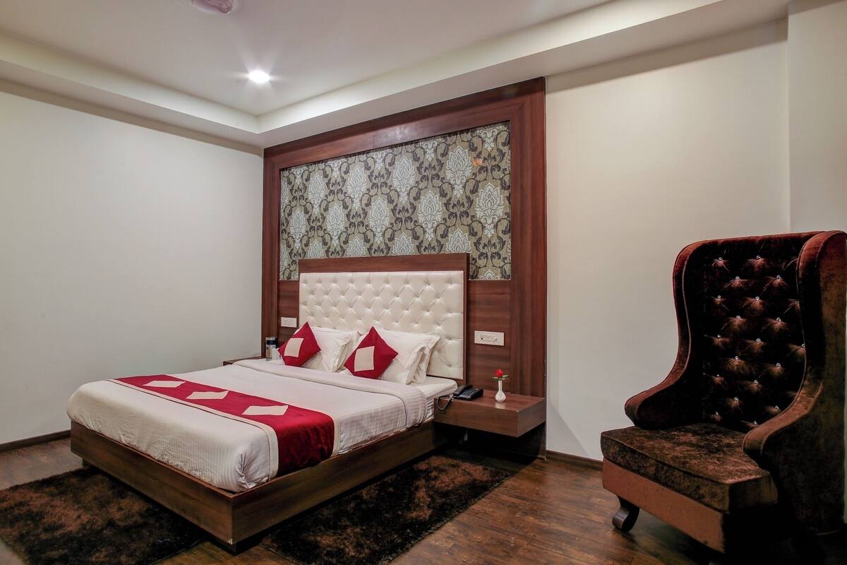 A bedroom with a large bed, a wooden headboard, a nightstand, a chair, and a patterned wallpaper.