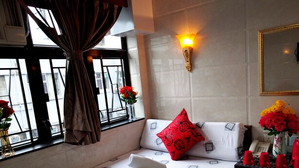 Quarto de hotel com cama, janela com cortinas, luminária na parede e um vaso com flores.