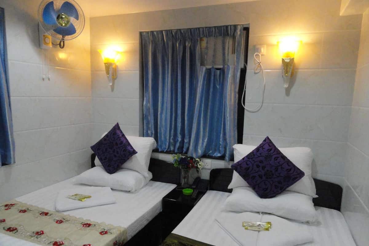 A hotel room with two single beds, a small table, a fan, and a window with curtains.