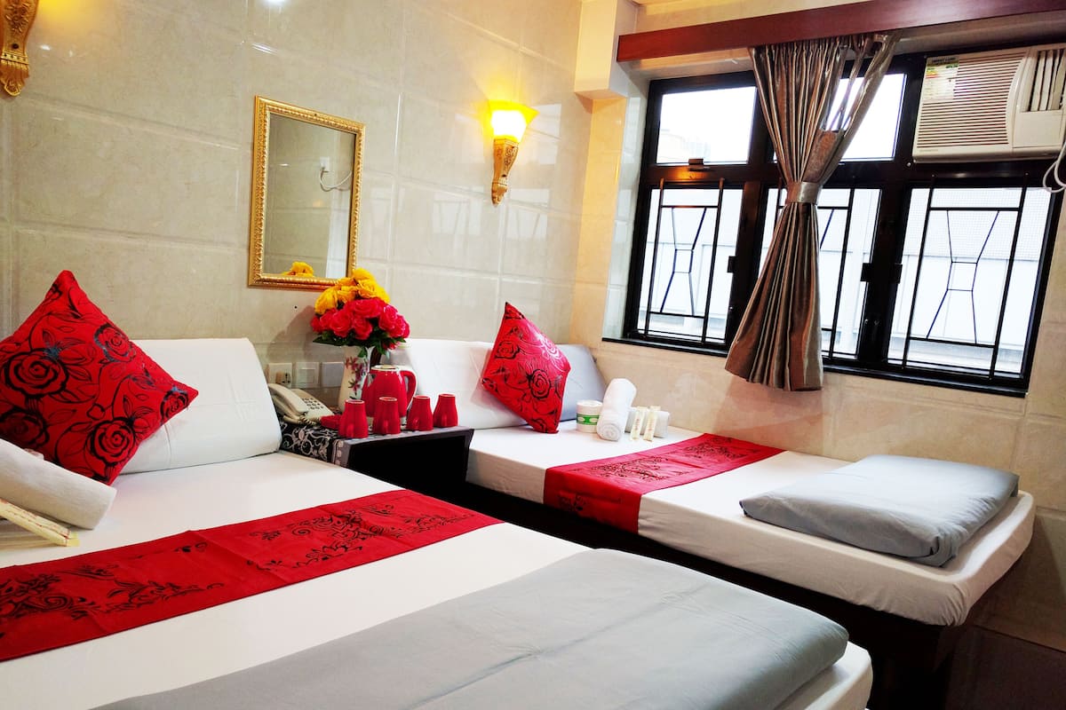 A hotel room with two beds, a mirror, a vase with flowers, and a window with curtains.