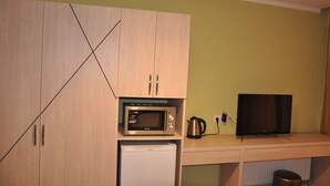 A compact kitchenette with a microwave, a small refrigerator, a kettle, and a television on a wooden countertop.