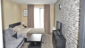 A hotel room with a bed, a sofa, a TV, and a stone-patterned wall.